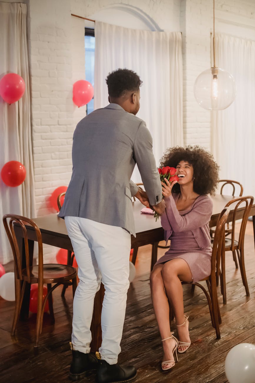 black man giving bouquet of roses to woman at table