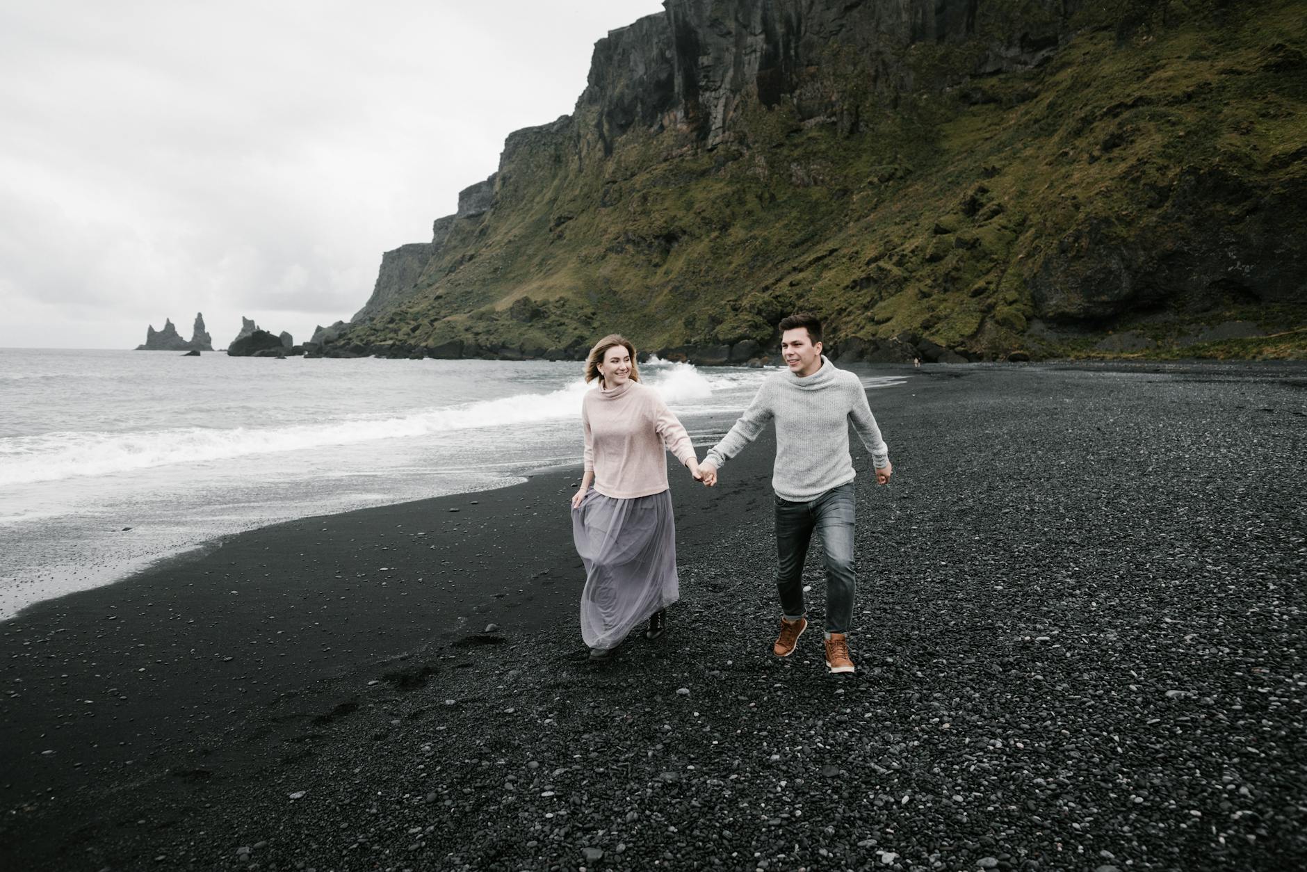 cheerful male and female running and holding hands on seashore